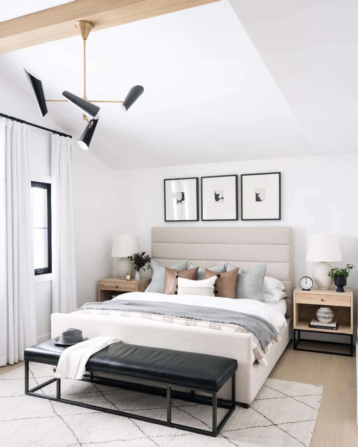 Chambre à coucher moderne avec des accents gris clair et marron. tapis blanc. Banc en cuir noir au bout du lit