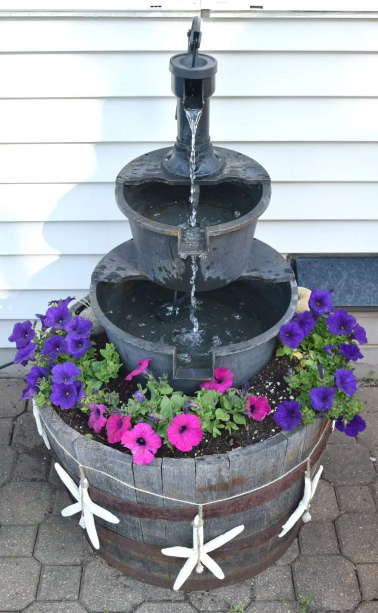 Une fontaine d'eau en cascade à trois niveaux avec des fleurs au fond.