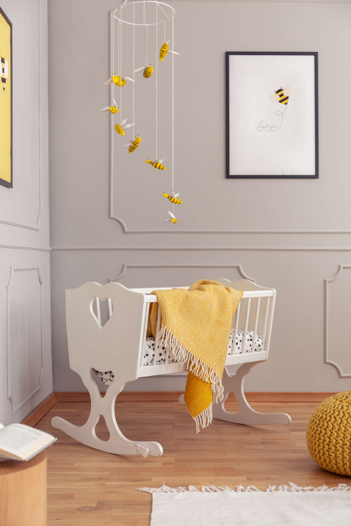 Bees above white wooden cradle in grey baby nursery with poster on the empty wall