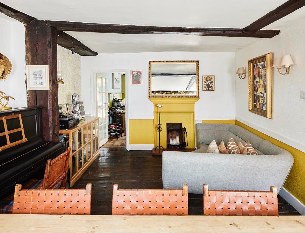 Un salon lumineux avec des poutres en bois foncé, des murs blancs et un élégant demi-mur jaune.