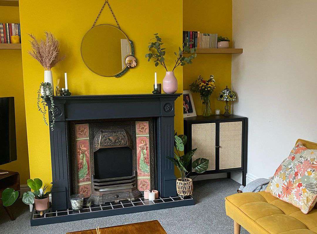 Un petit salon avec un mur d'accent jaune vif et un manteau de cheminée noir spectaculaire.