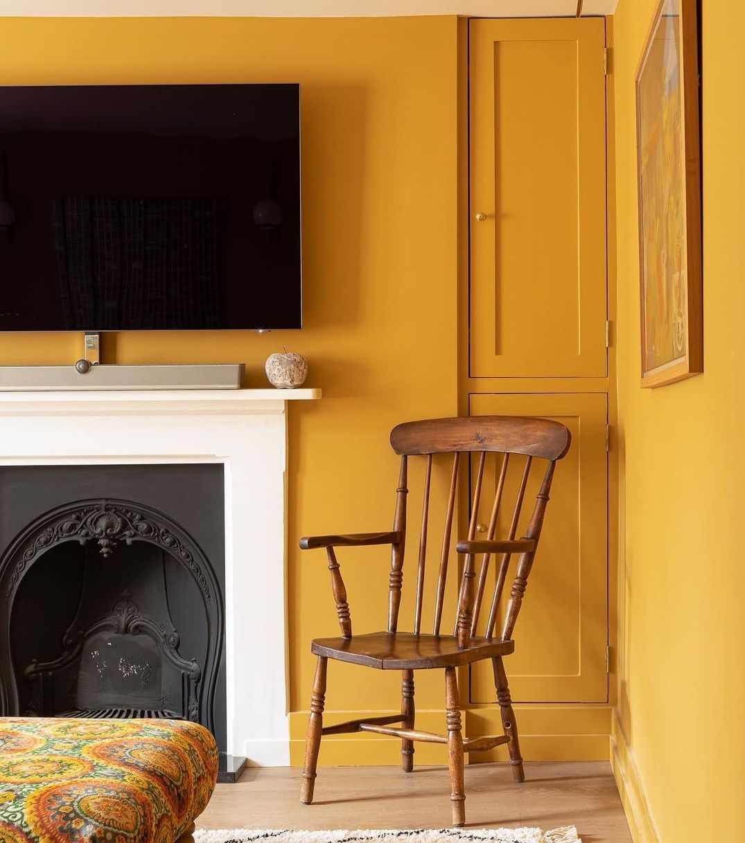 Un salon peint en jaune moutarde avec une cheminée blanche.