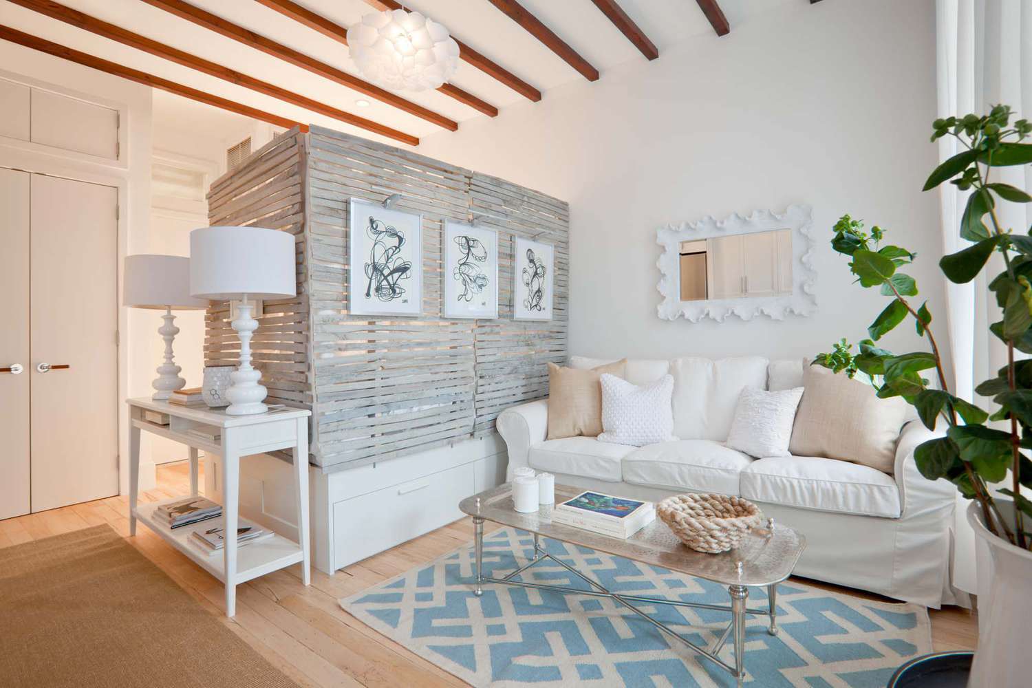 Studio de ferme moderne avec canapé blanc, tapis bleu et blanc, table d'appoint avec deux lampes et table basse.