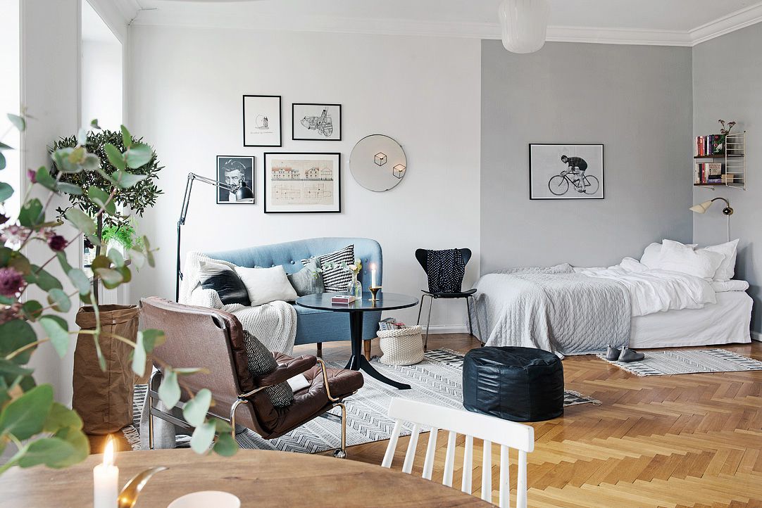 Mur-galerie dans un studio avec lit, canapé bleu et table en verre.