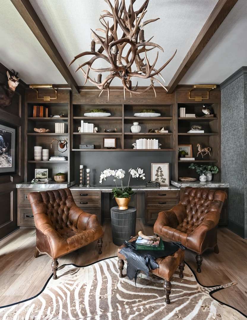 Lustre en bois de cerf dans un bureau rustique moderne avec des chaises en cuir et des encastrements en bois.
