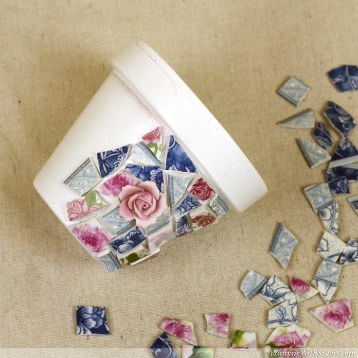 Un pot de fleurs blanc recouvert de morceaux de mosaïque de porcelaine brisée.