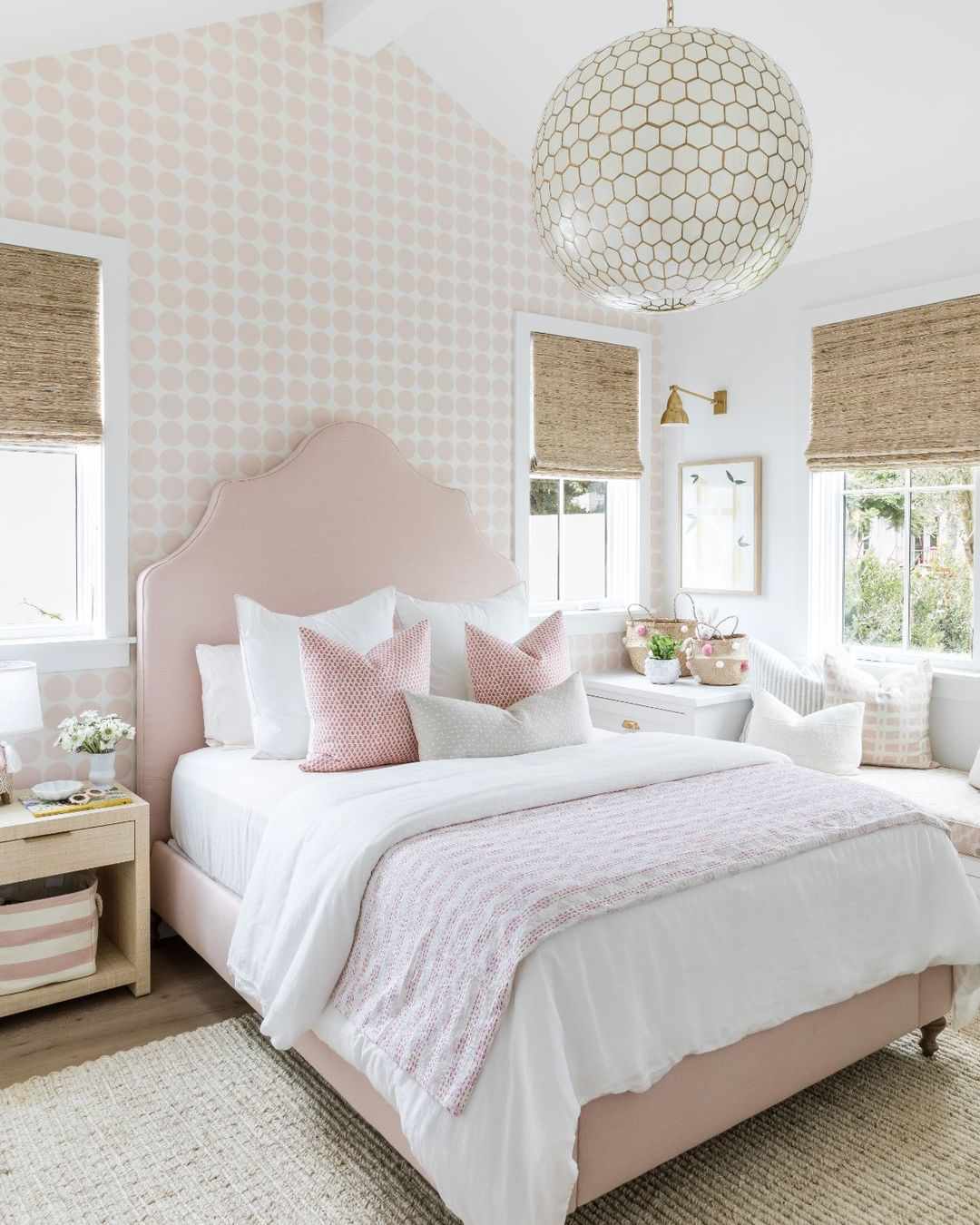 Une chambre d'adolescente avec une tête de lit et une literie roses et une grande lampe suspendue ronde au-dessus du lit.
