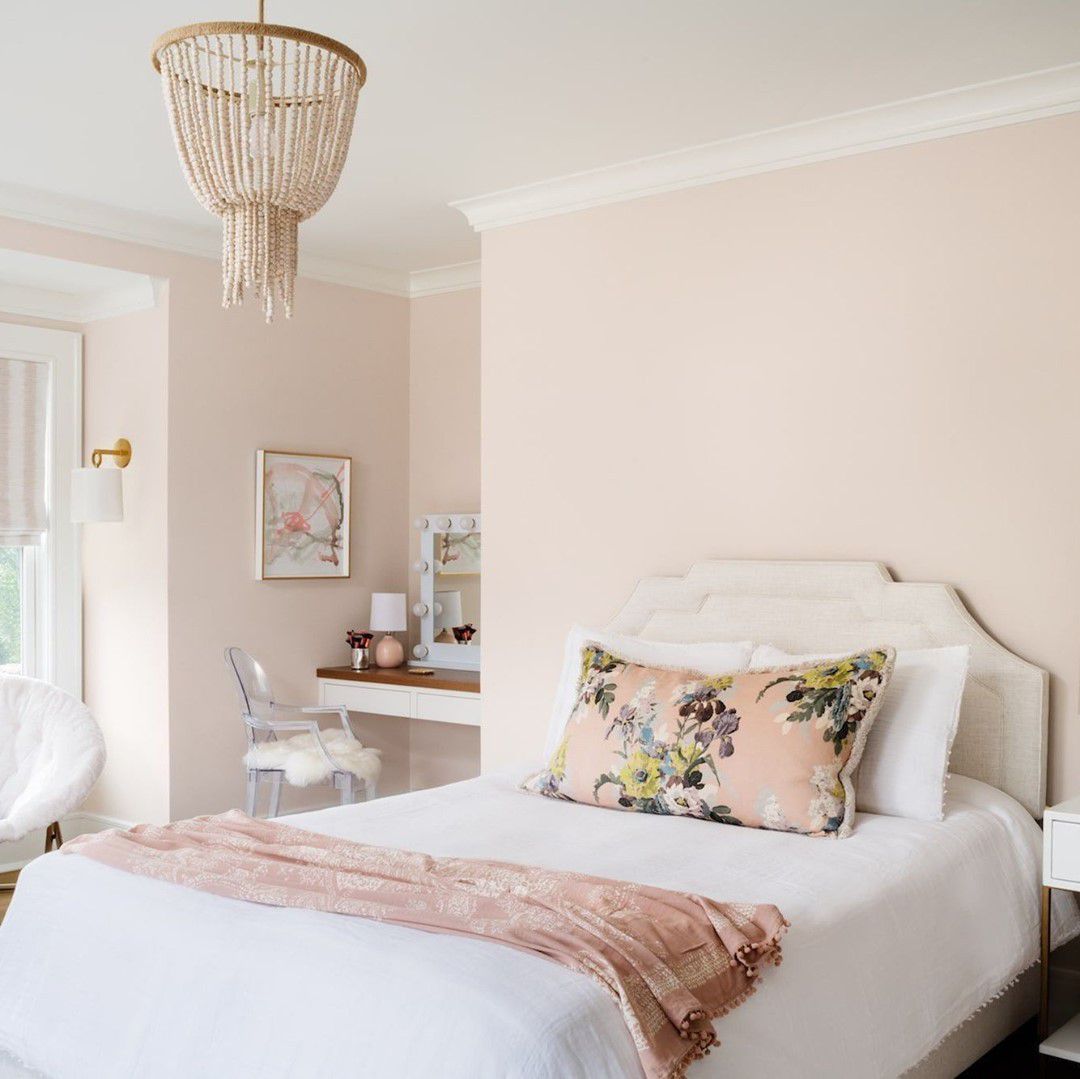 Une chambre d'adolescente toute en rose avec un espace pour les devoirs et un coussin fleuri sur le lit.