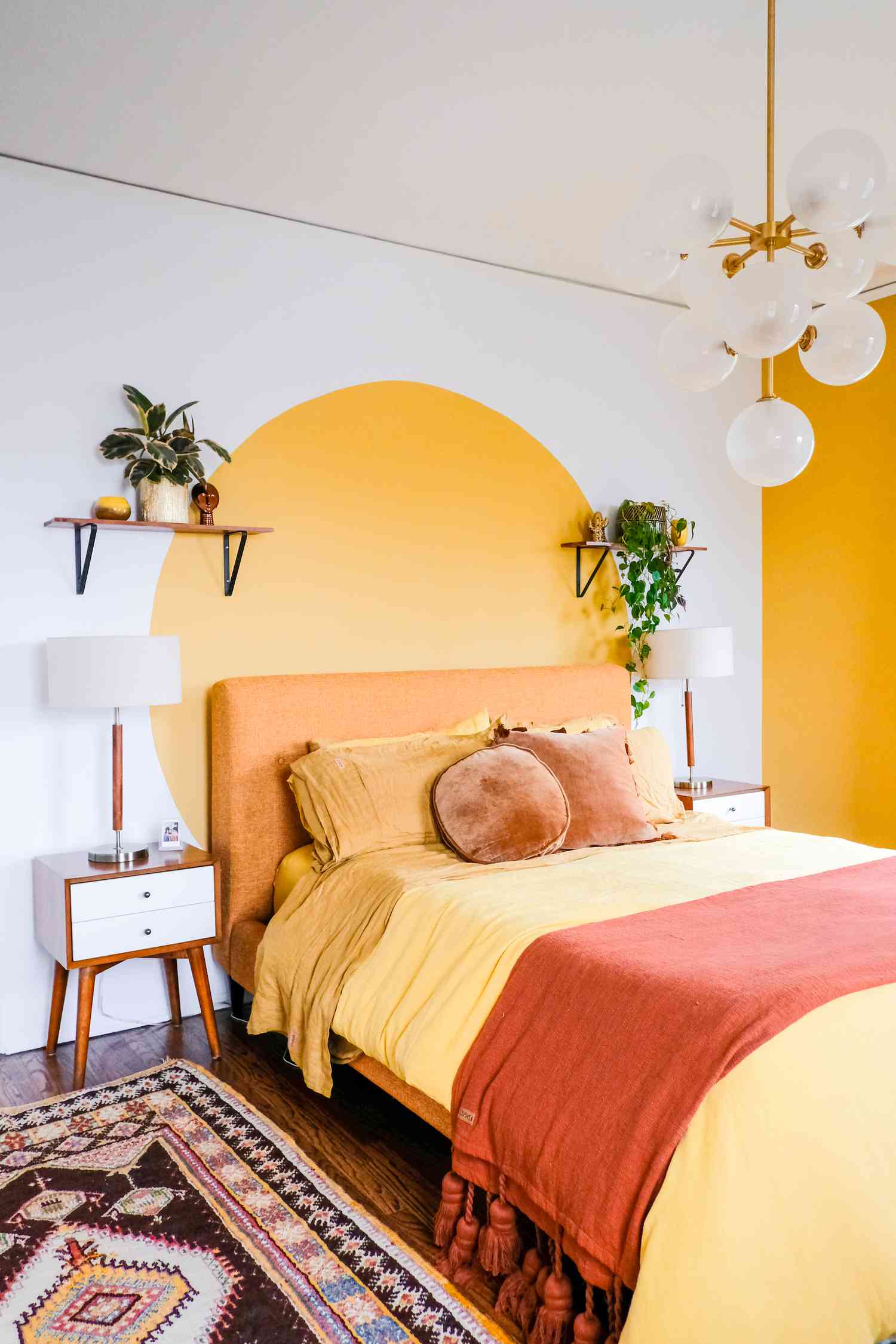 Une chambre à coucher lumineuse et gaie avec un cercle jaune vif sur le mur, un lit et une literie jaunes et un lustre à bulles.