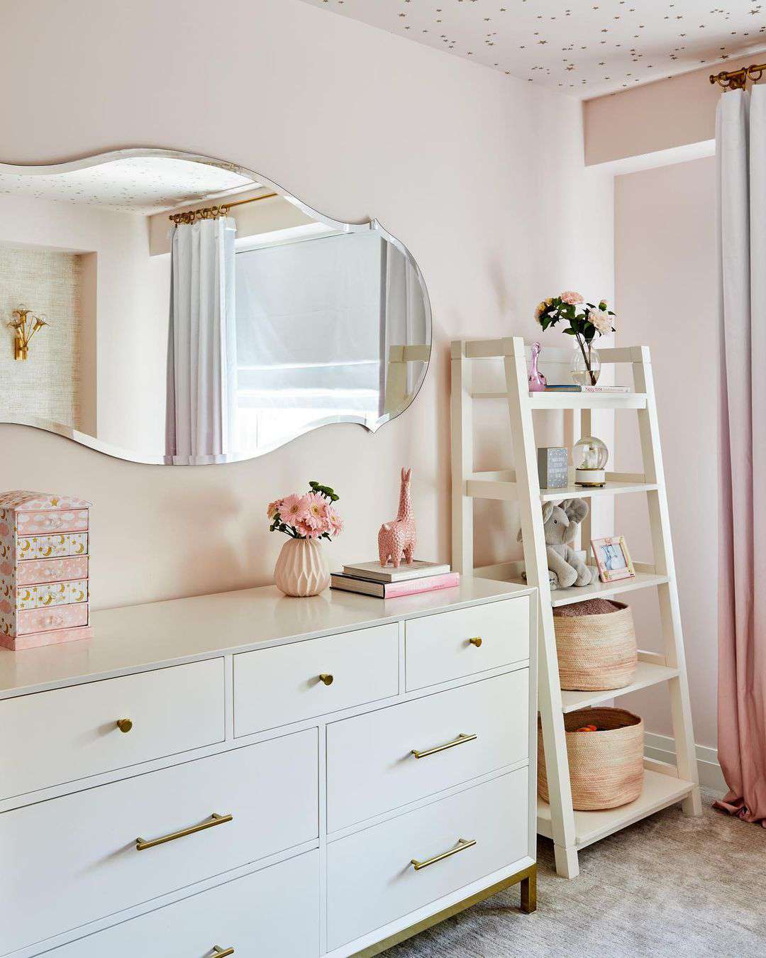 Un coin dans la chambre d'une adolescente avec une étagère en échelle, une commode blanche et un miroir orné.