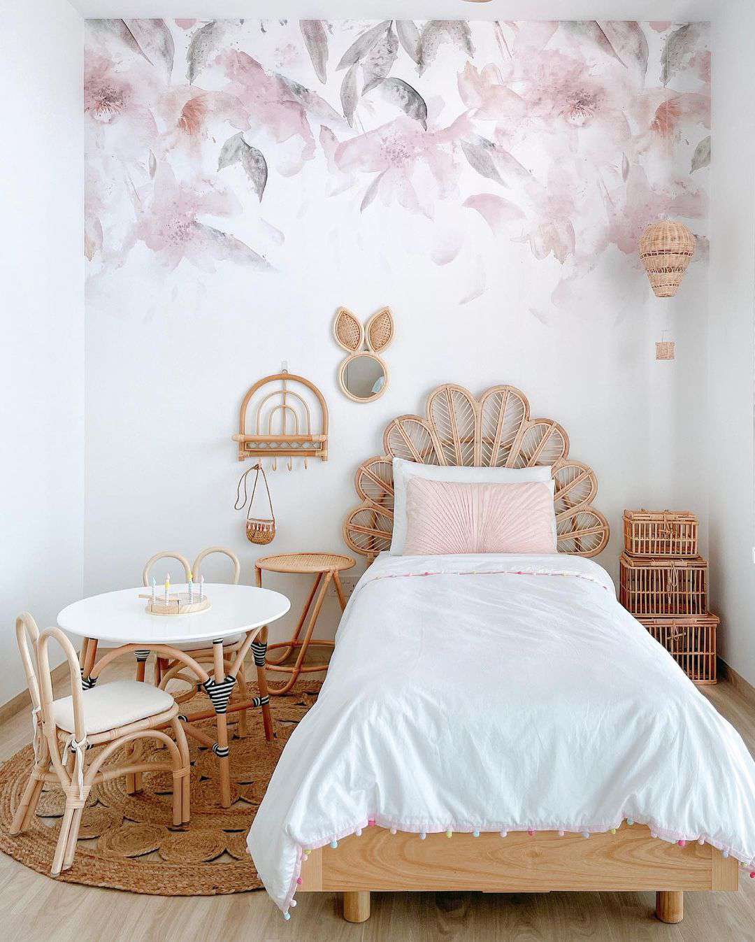 Une adorable chambre d'adolescente avec un mur floral en aquarelle, des meubles en rotin et une sculpture de montgolfière en rotin suspendue.
