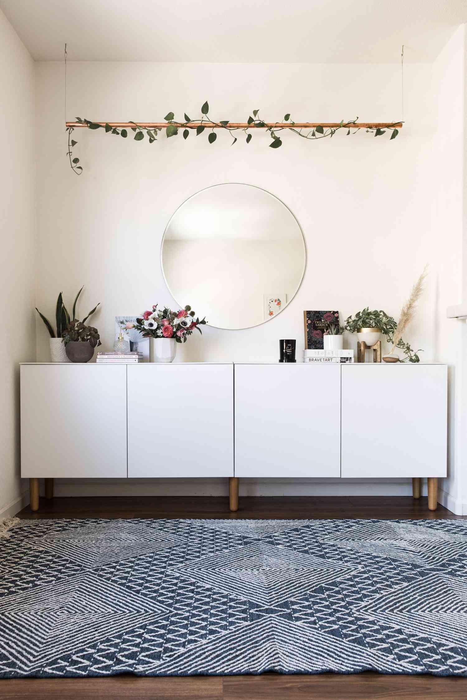 Un coin dans la chambre d'une adolescente avec de la verdure suspendue, un miroir rond, une table de buffet blanche et des plantes et des fleurs fraîches.