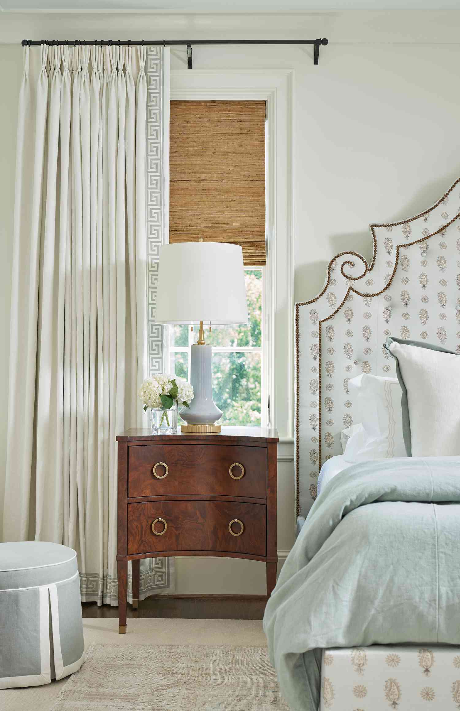 Chambre à coucher avec tête de lit capitonnée, table de nuit en bois et fenêtre