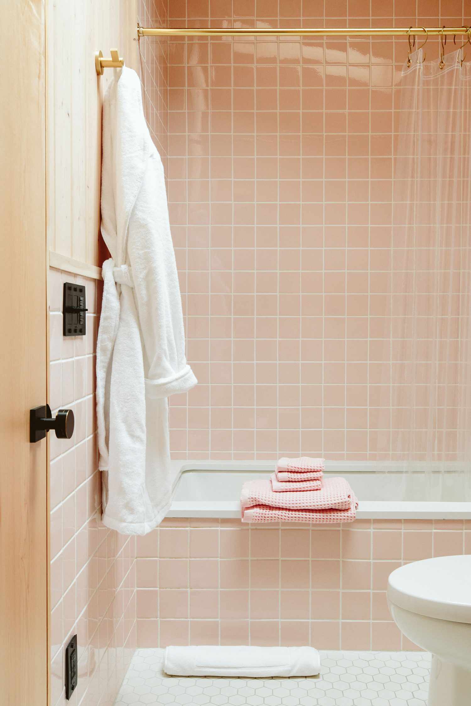 Un carrelage de salle de bains rose layette est associé à un sol et à une porte en carreaux beiges.