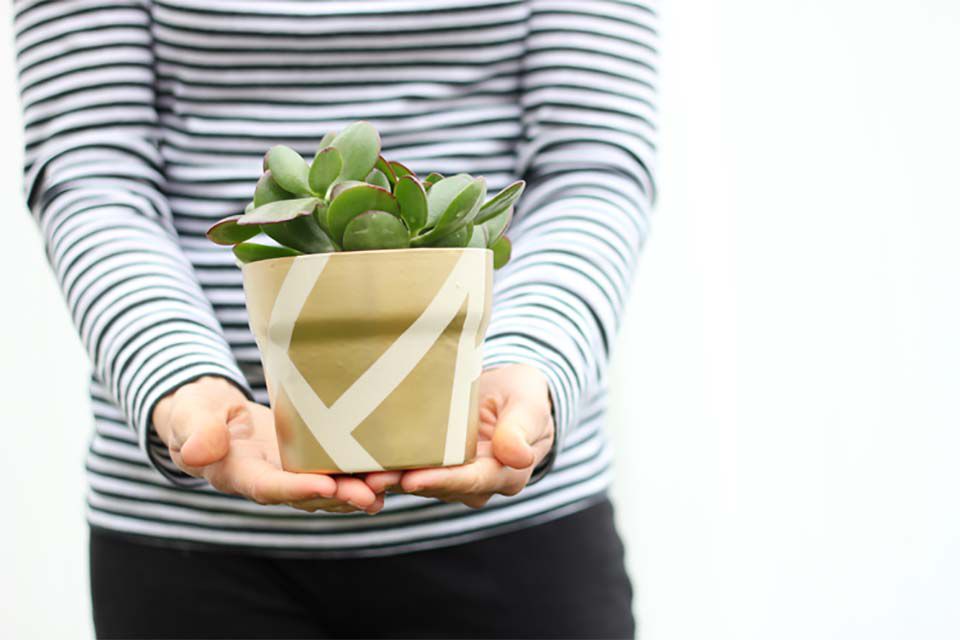 Une femme tenant un pot doré contenant une plante.