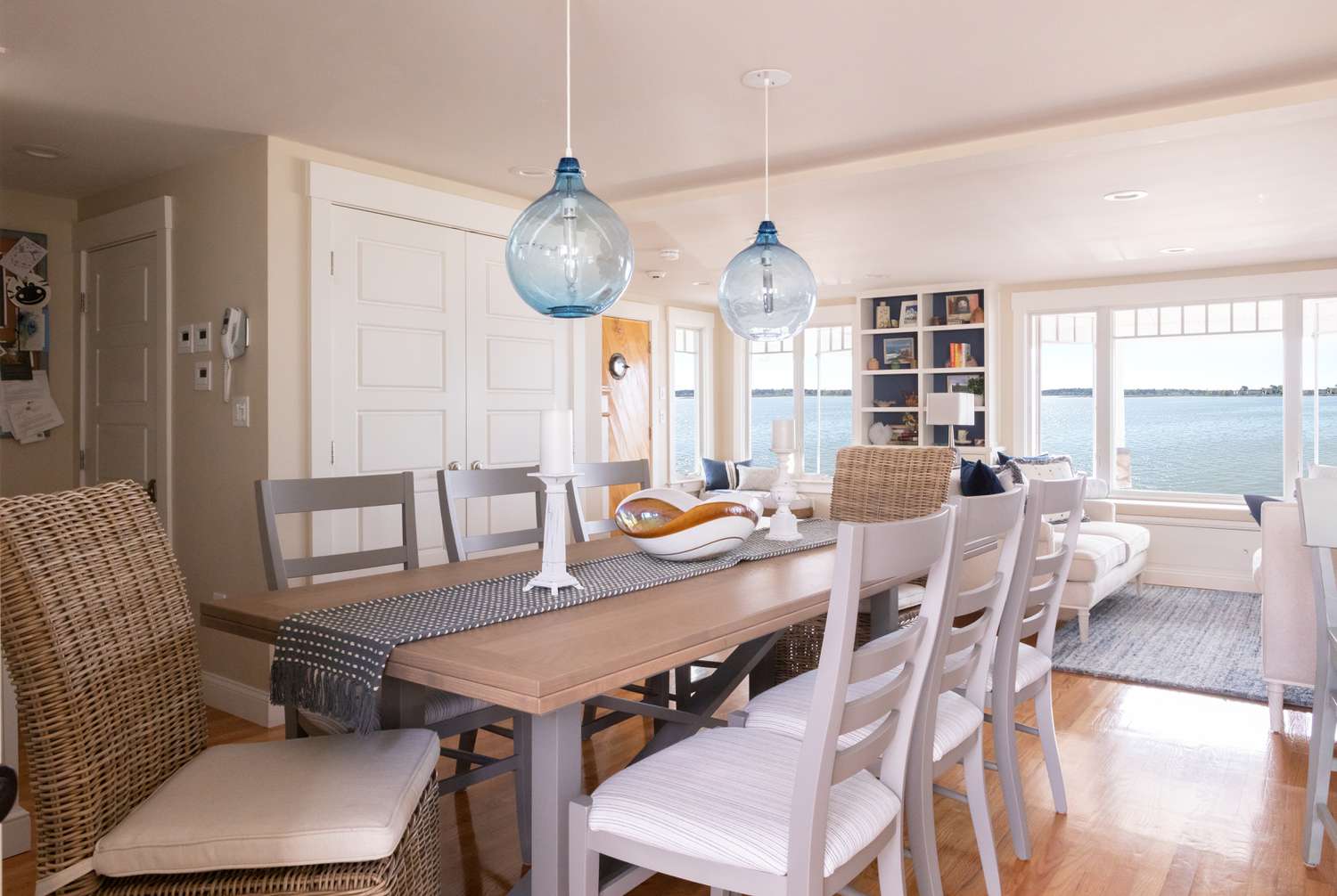 Dans une salle à manger, de grands luminaires en verre bleu sont suspendus au-dessus d'une table en bois clair,