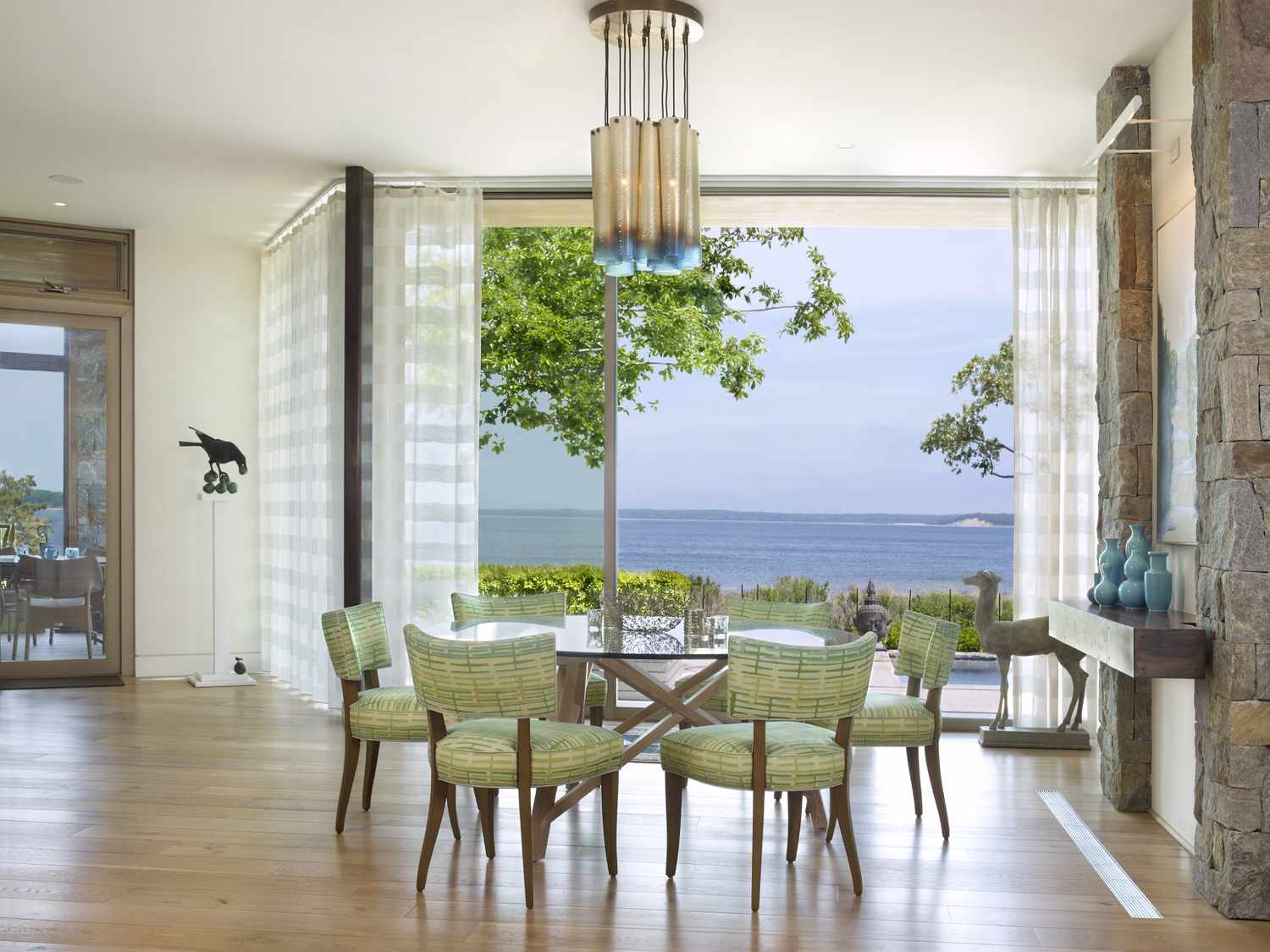 Une grande baie vitrée donne sur la mer, tandis qu'à l'intérieur, des chaises safran entourent une table en verre.