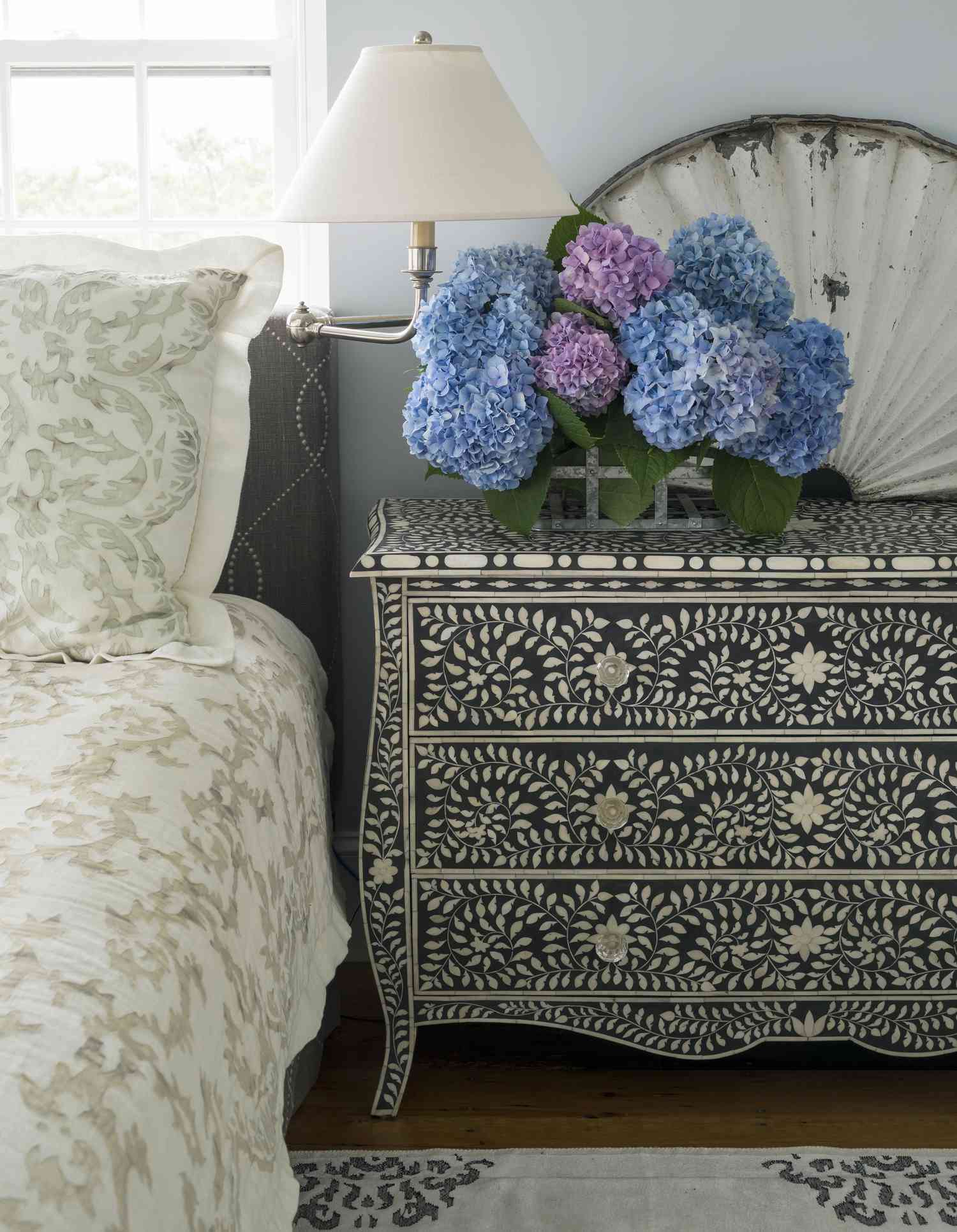 Gros plan sur des hortensias posés sur une table d'appoint à côté d'un lit.