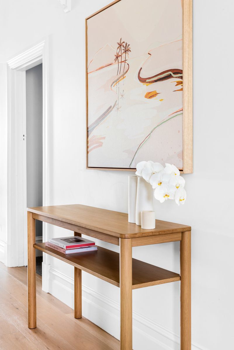 Une peinture de bord de mer dans un cadre en bois moderne est suspendue au-dessus d'une table d'appoint.