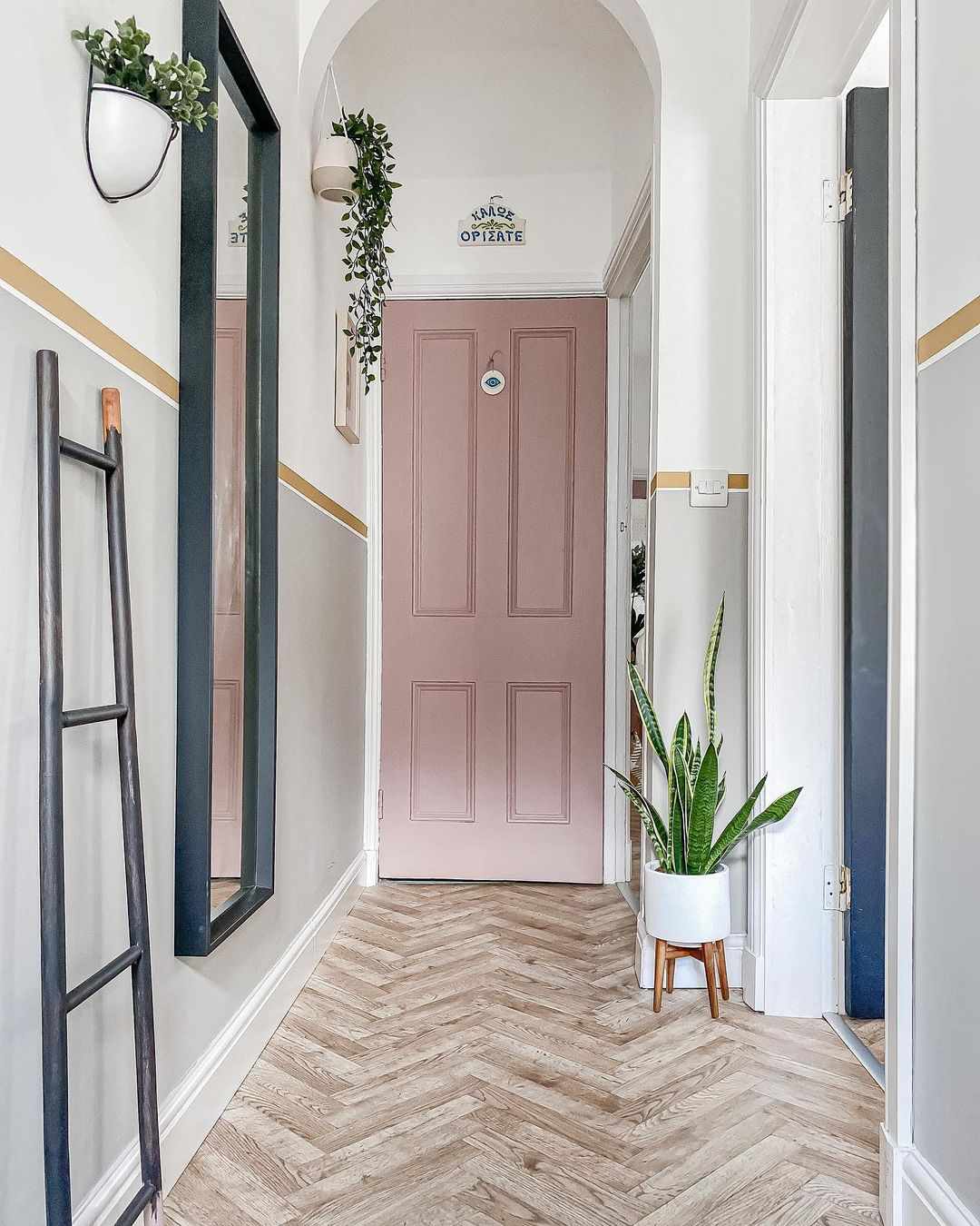 Couloir étroit avec des plantes au mur, un miroir suspendu et une échelle penchée.