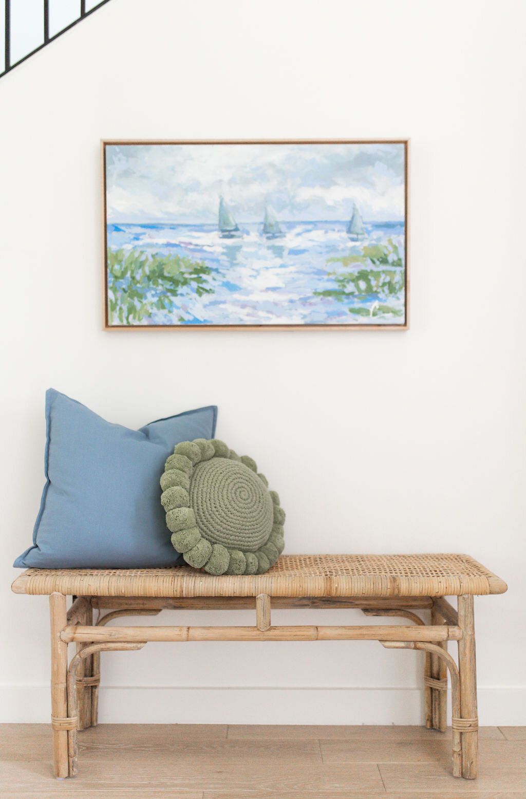 Banc en osier avec des coussins et une œuvre d'art au-dessus.