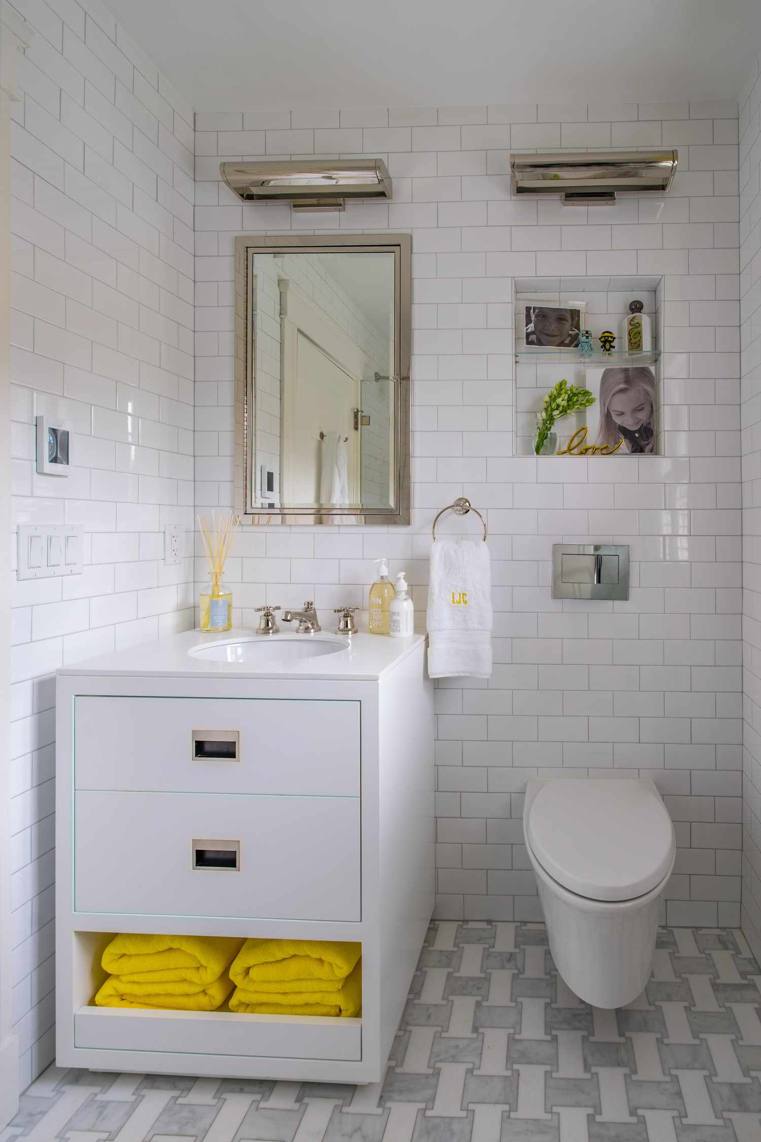 Salle de bain blanche avec des carreaux de métro, des accessoires chromés, des serviettes et des accessoires jaunes. 