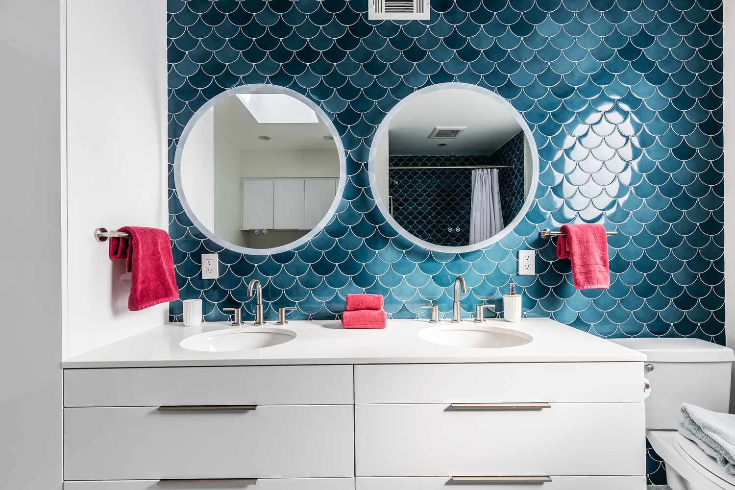 Salle de bains pour enfants avec des murs bleus en forme d'écailles de poisson, des miroirs circulaires et des serviettes rouges.