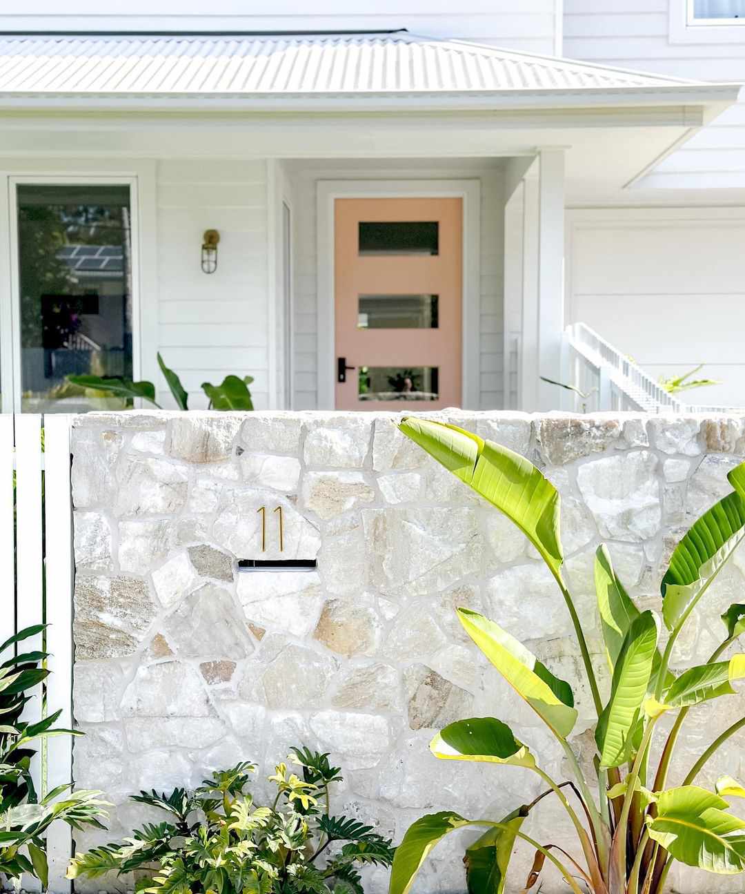Porte rose sur maison blanche avec clôture en pierre