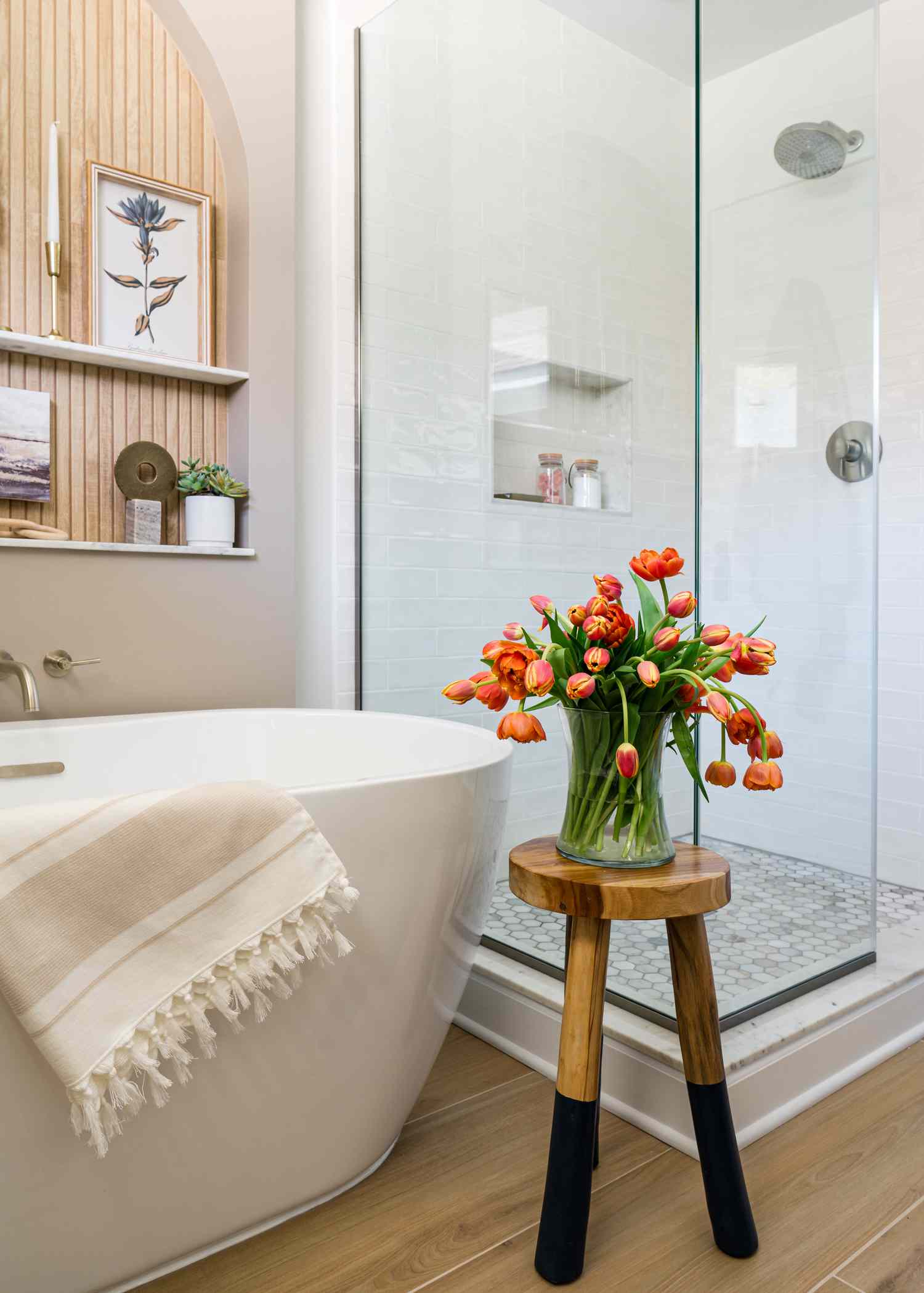 Le sol en bois accueille une baignoire blanche lisse avec une douche en verre à proximité.
