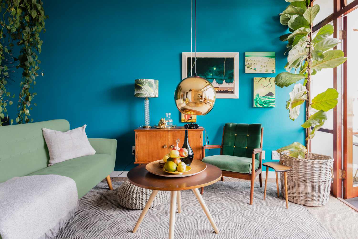 Salon avec des murs couleur sarcelle, des sièges vert clair et des meubles en bois recouverts de plantes d'intérieur.