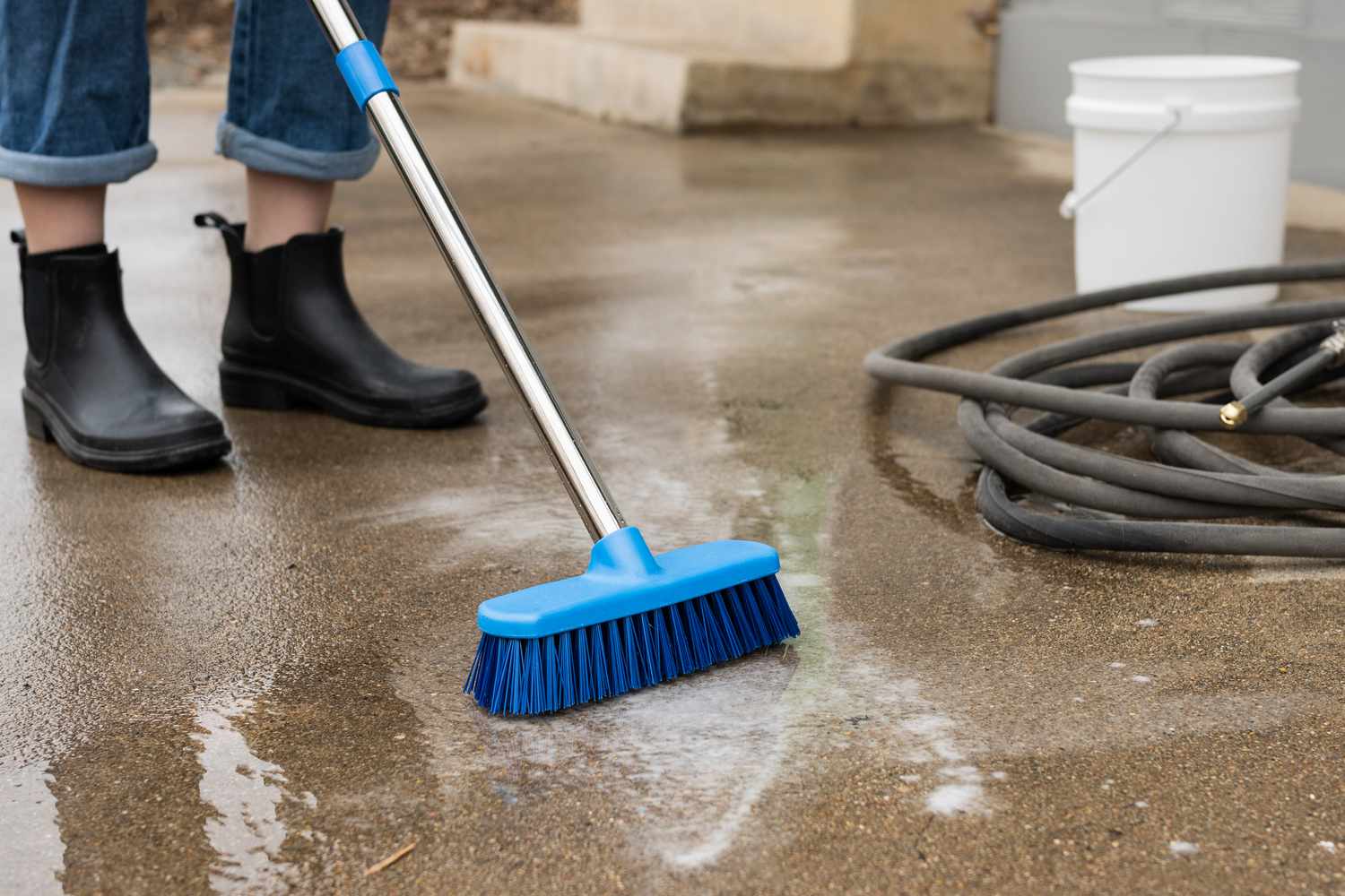 Balai à poils de nylon frottant une solution de nettoyage sur une terrasse en béton non scellée.