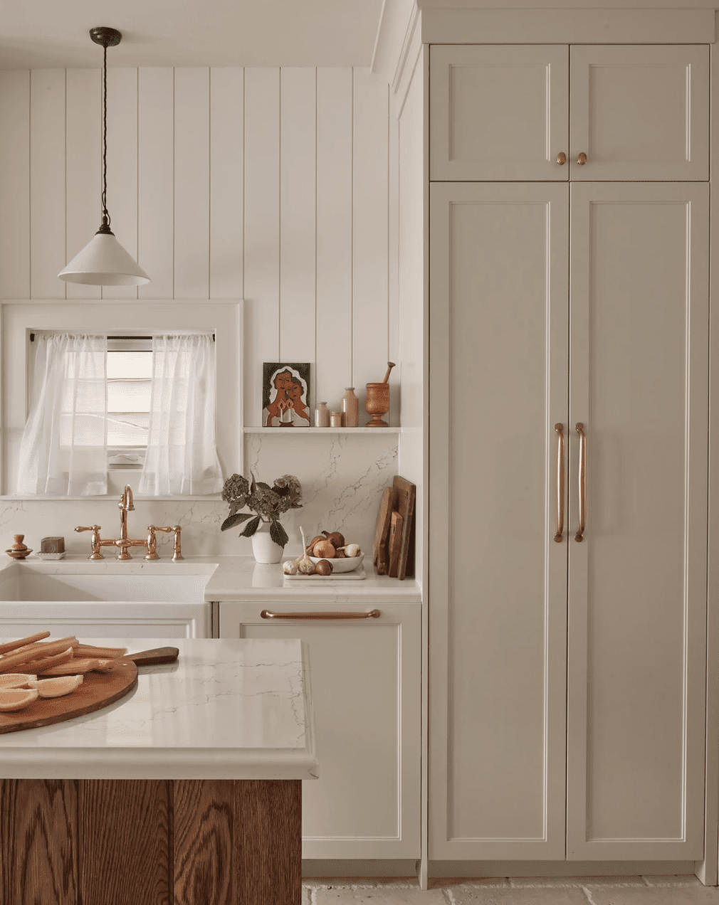 Une cuisine remplie de blanc avec une petite fenêtre entourée de stores et de rideaux