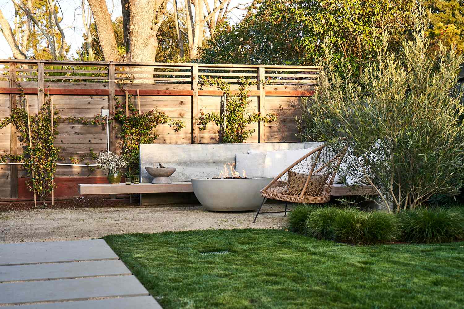 Jardin tranquille avec bol de feu en béton et lianes plantées le long de la clôture