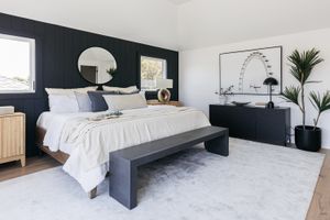 Decorated bedroom with navy blue walls, dresser and bench surrounding a white bed
