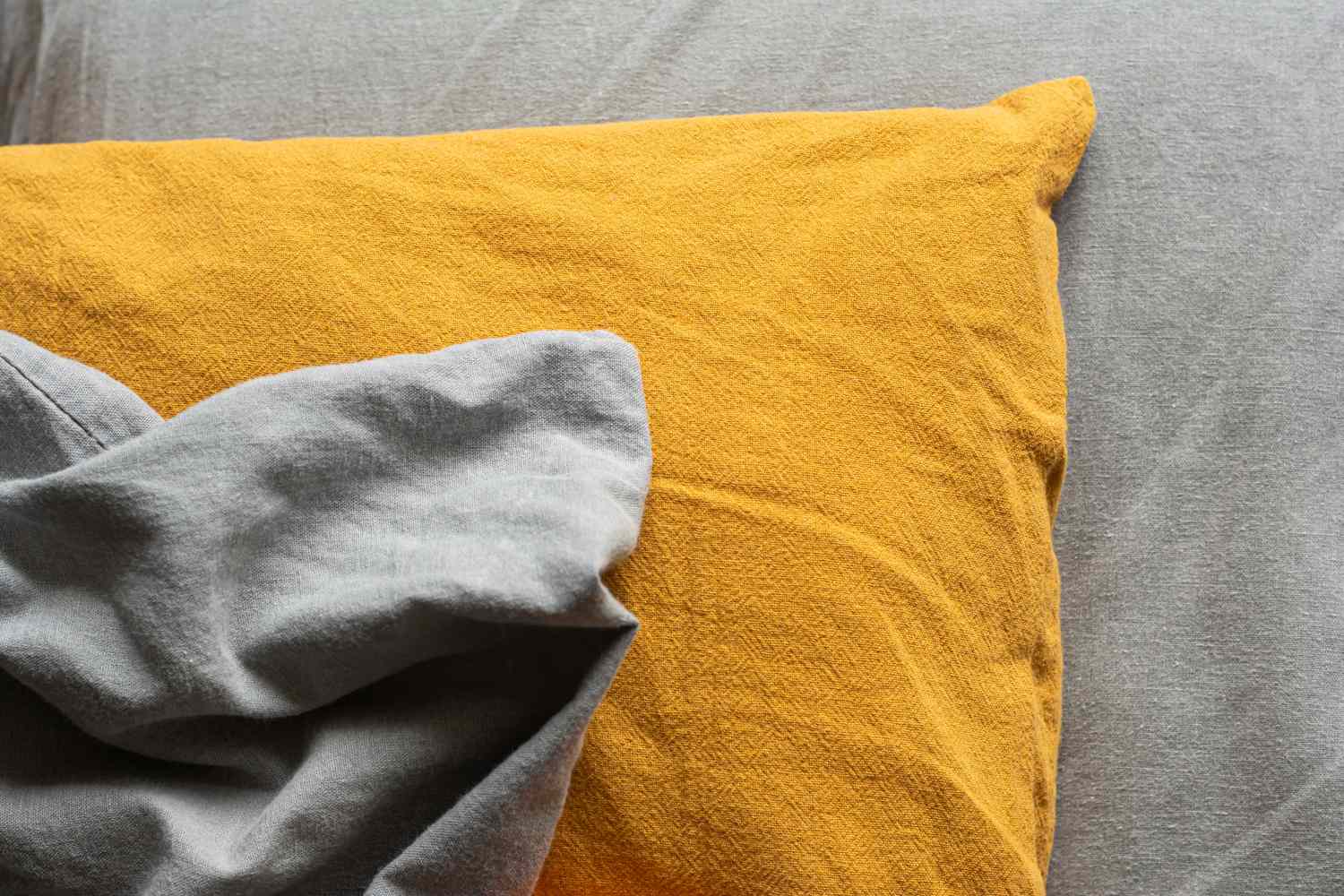 Une taie d'oreiller texturée sur un drap gris.